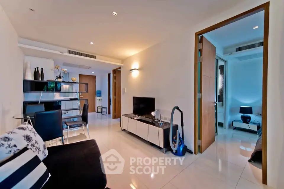 Modern living room with sleek furniture and open layout, leading to a cozy bedroom.