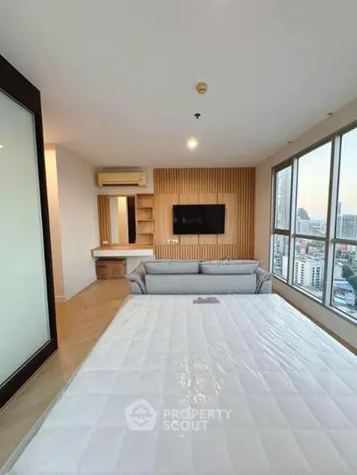 Modern bedroom with city view, featuring a cozy bed, wall-mounted TV, and large windows for natural light.