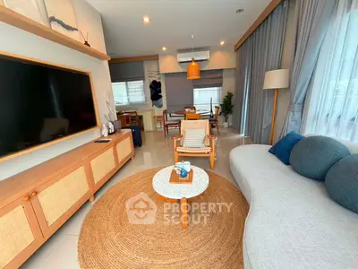 Modern living room with stylish furniture and large TV, featuring natural light and cozy decor.