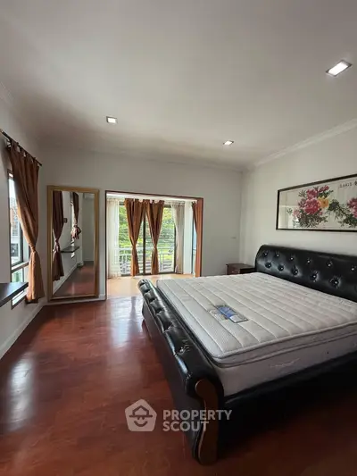 Spacious bedroom with elegant wooden flooring and large windows for natural light.