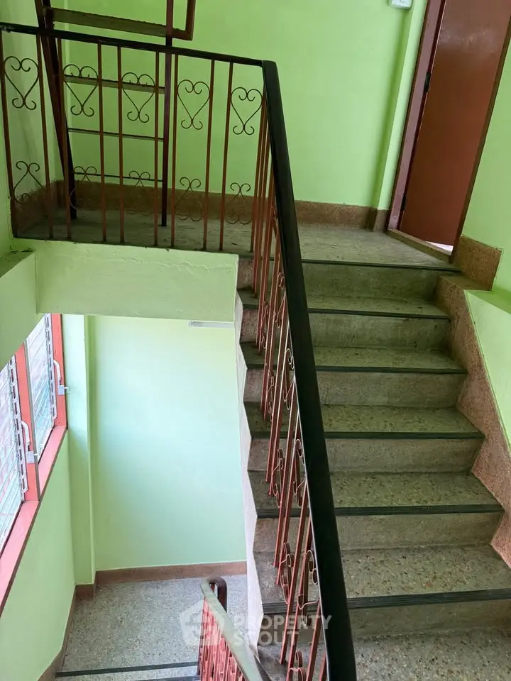 Charming staircase with vintage railing in a well-lit building interior, perfect for cozy urban living.