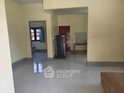Spacious living area with tiled flooring and natural light, featuring a refrigerator and open layout.