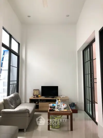 Modern living room with high ceilings and sleek furniture, featuring a cozy sofa and entertainment setup.