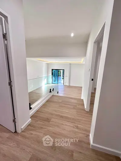 Spacious modern interior with wooden flooring and glass railing, leading to a bright living area.