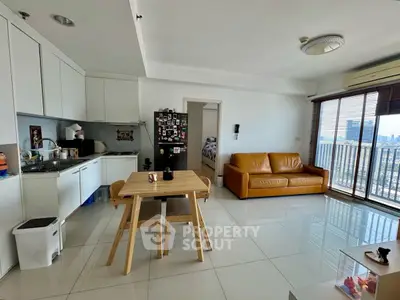 Modern open-plan living room with kitchen, featuring a cozy sofa and city view balcony.