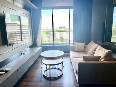 Modern living room with large window and city view, featuring a sleek TV setup and comfortable seating.
