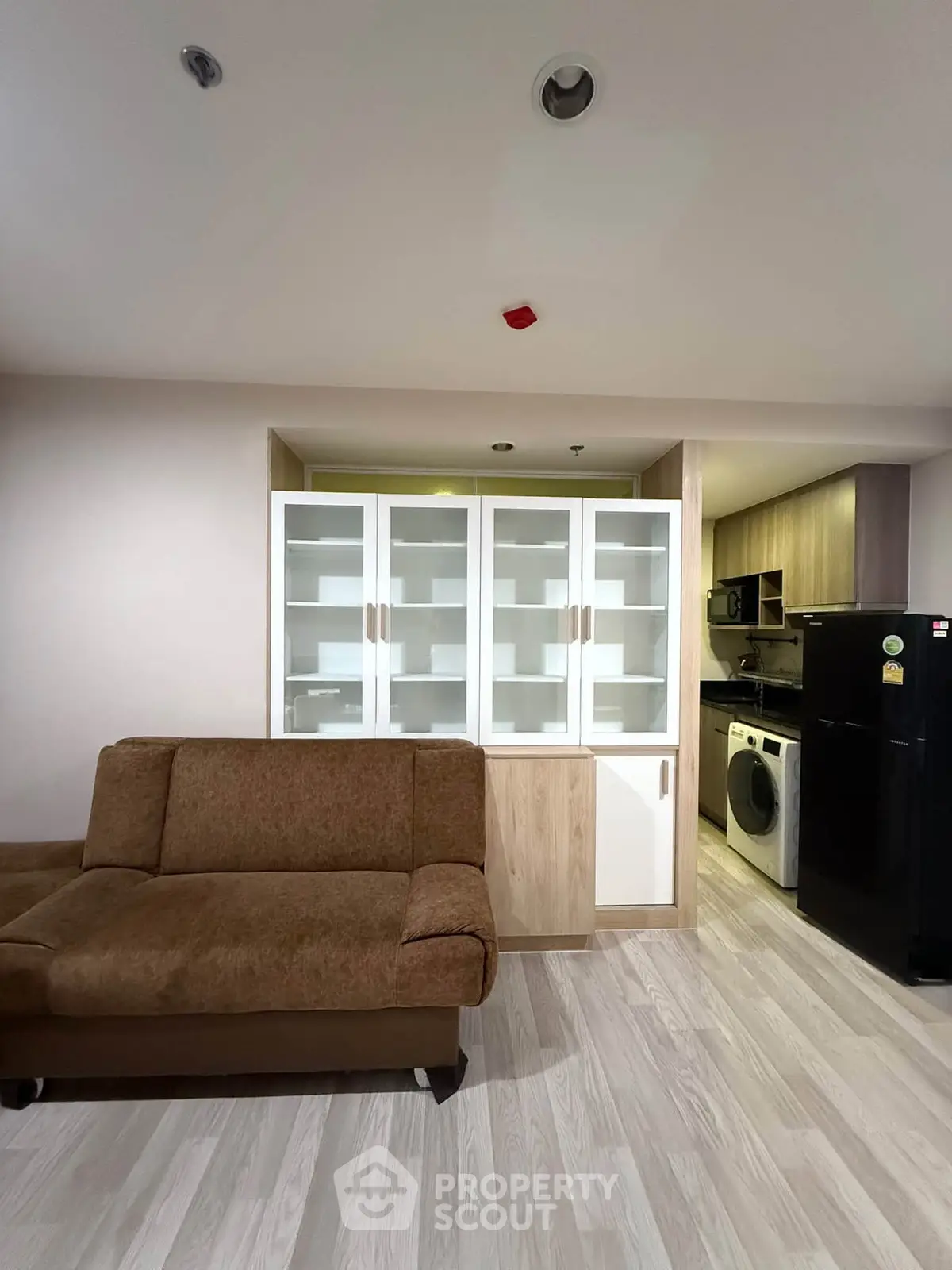 Modern living room with stylish sofa and built-in shelving, adjacent to a compact kitchen with appliances.