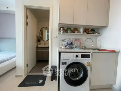 Modern apartment interior with compact kitchen and washing machine, adjacent to a cozy bedroom and bathroom.