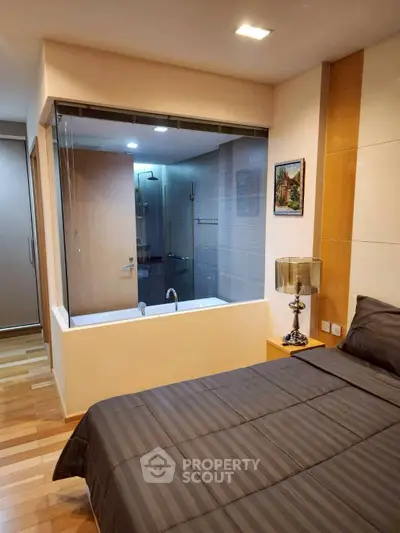 Modern bedroom with glass wall overlooking stylish bathroom and wooden flooring.