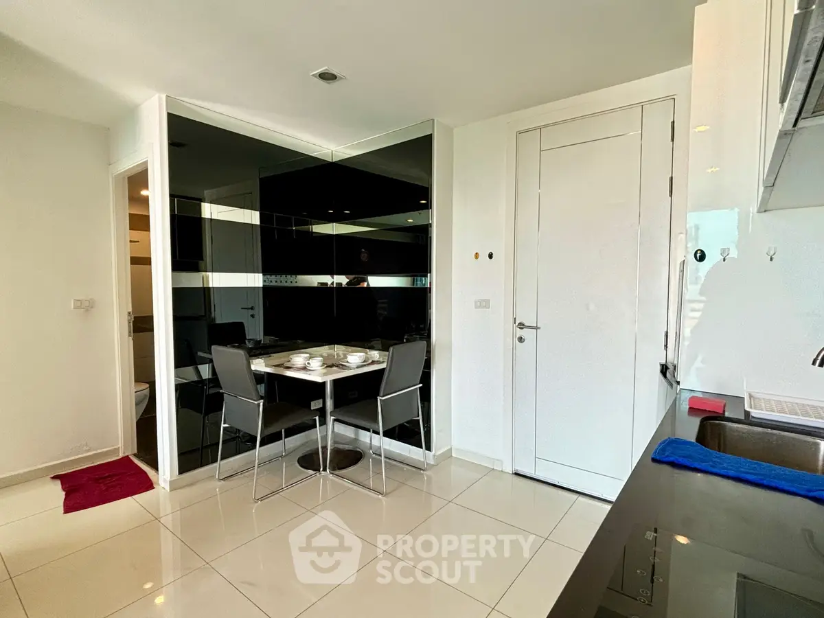 Modern kitchen with sleek black and white design, featuring a dining area and glossy tiled floor.