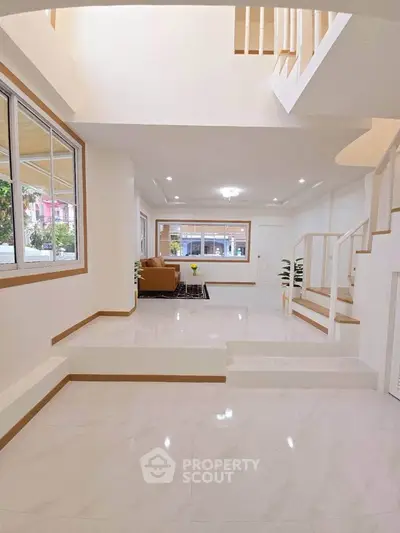 Spacious modern living room with elegant staircase and large windows.