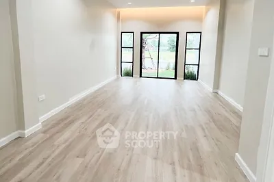 Spacious and well-lit living room with elegant hardwood flooring and modern French doors leading to a serene outdoor view, perfect for a chic and comfortable lifestyle.