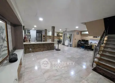 Spacious open-plan living area with modern decor and tiled flooring, featuring a staircase and home office setup.