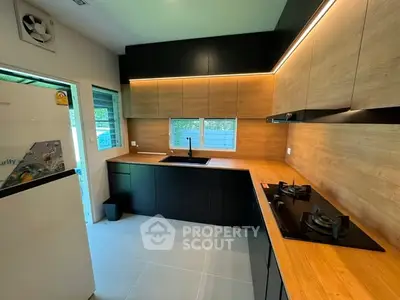 Modern kitchen with sleek black cabinets and wooden countertops, featuring a gas stove and ample natural light.