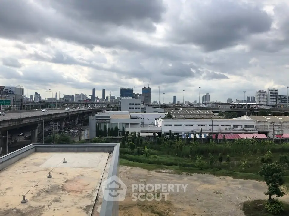 Urban skyline view with highway and industrial buildings under cloudy sky.