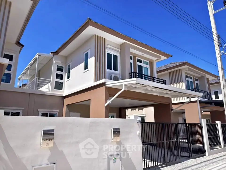 Modern two-story house with sleek design and gated entrance under clear blue sky.