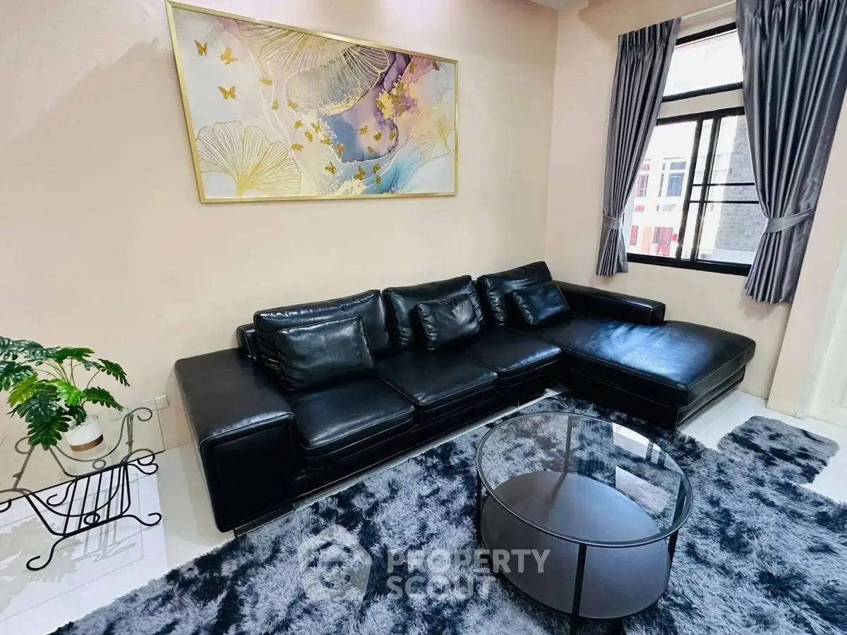 Modern living room with black leather sofa, stylish rug, and large window for natural light.