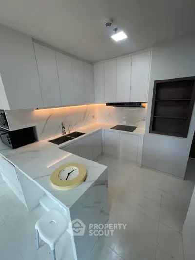 Modern kitchen with sleek white cabinetry and marble countertops, featuring an open layout and integrated appliances.