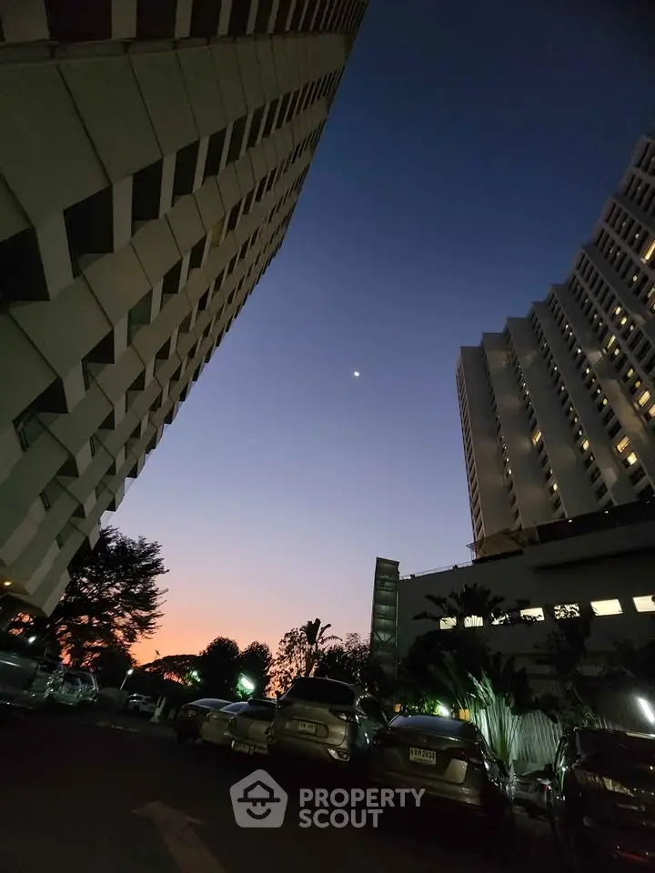 Stunning twilight view of modern high-rise buildings with parked cars, showcasing urban architecture.