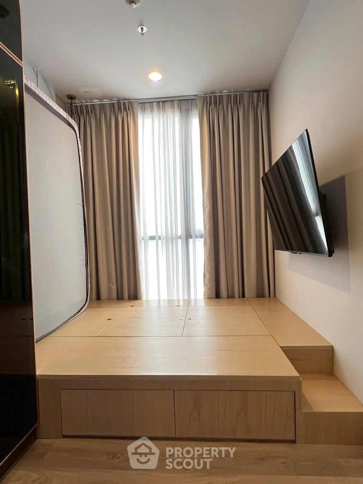 Modern minimalist bedroom with platform bed and wall-mounted TV, featuring elegant curtains and wooden flooring.