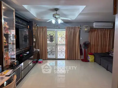 Spacious living room with modern decor, large TV, and ample natural light from glass doors.