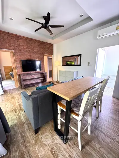 Charming living room with rustic brick wall, modern ceiling fan, and cozy seating area, perfect for relaxation.