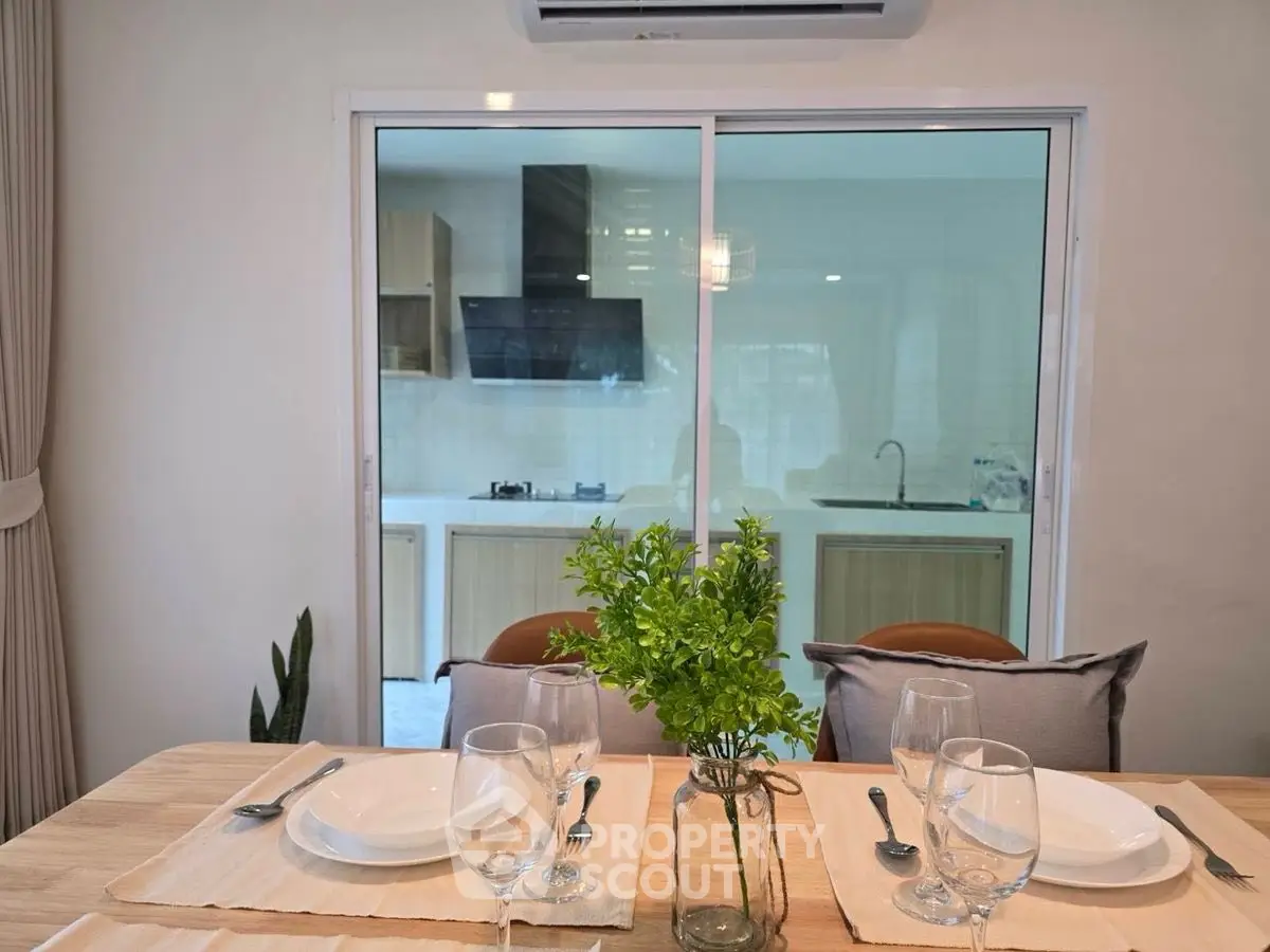 Modern dining area with view into sleek kitchen through glass doors.