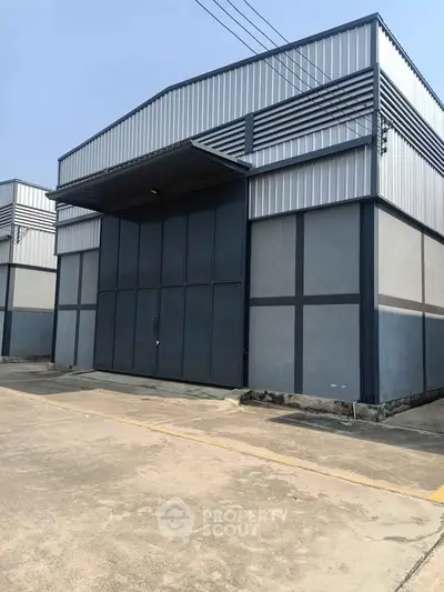 Modern industrial warehouse exterior with large metal doors and spacious concrete driveway.