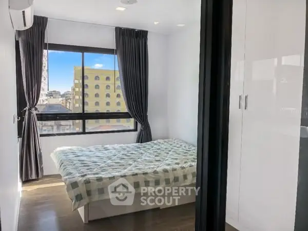 Modern bedroom with large window and city view, featuring sleek white wardrobe and cozy bed.