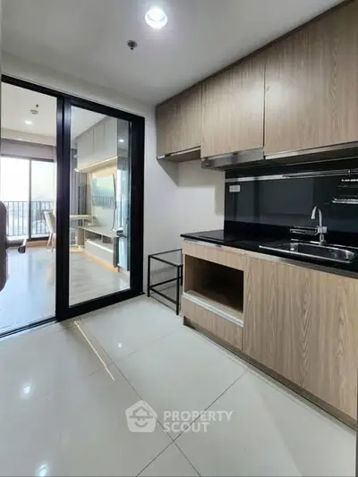 Modern kitchen with sleek cabinetry and open layout leading to bright living area with balcony view.