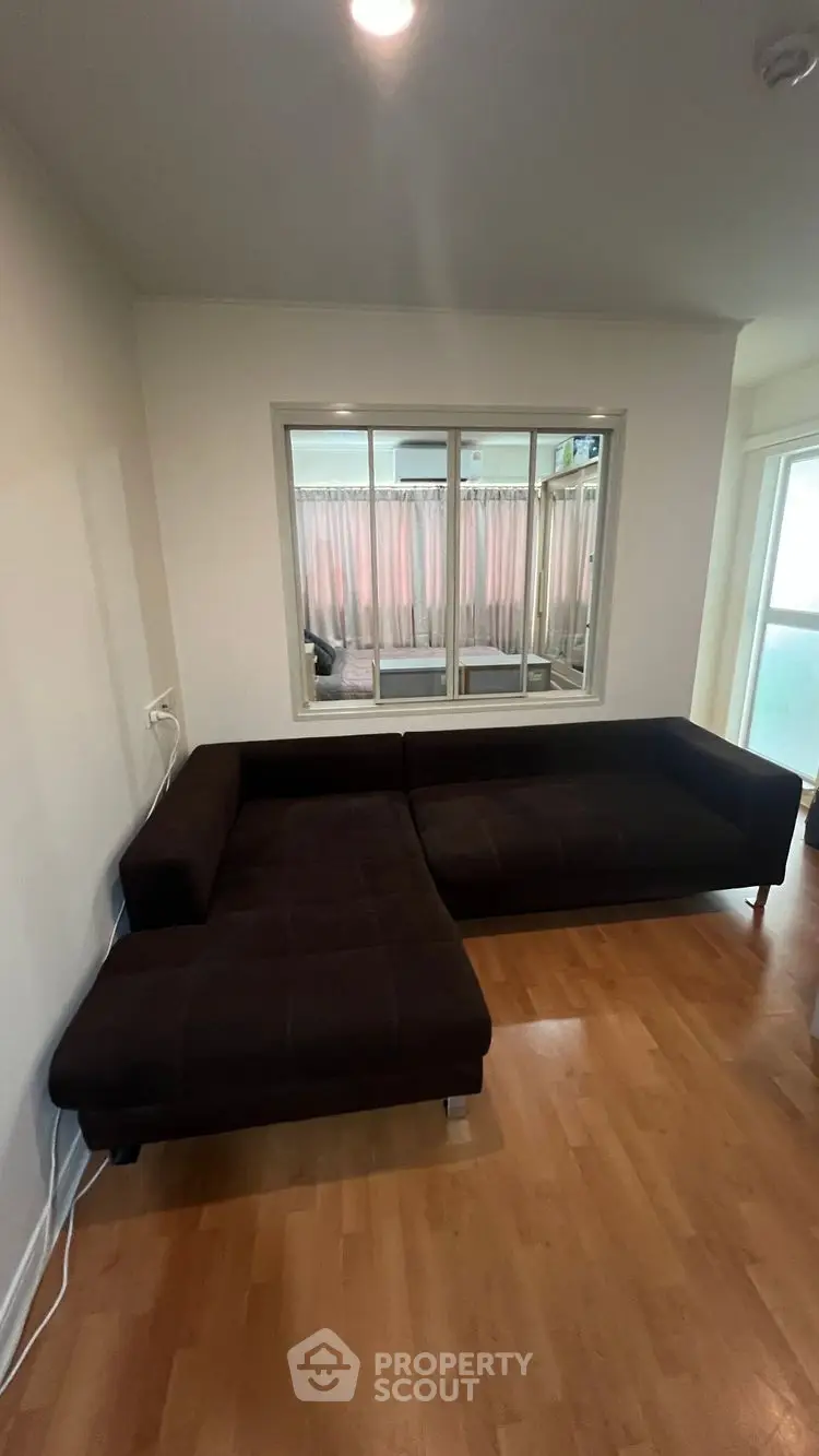 Cozy living room with dark sectional sofa and wooden flooring, perfect for relaxation.