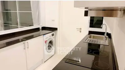 Modern kitchen with sleek black countertops and built-in appliances, featuring a washing machine and electric stove.