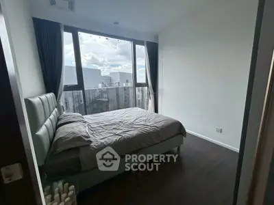 Modern bedroom with large windows offering stunning city views, featuring a cozy bed and sleek design.