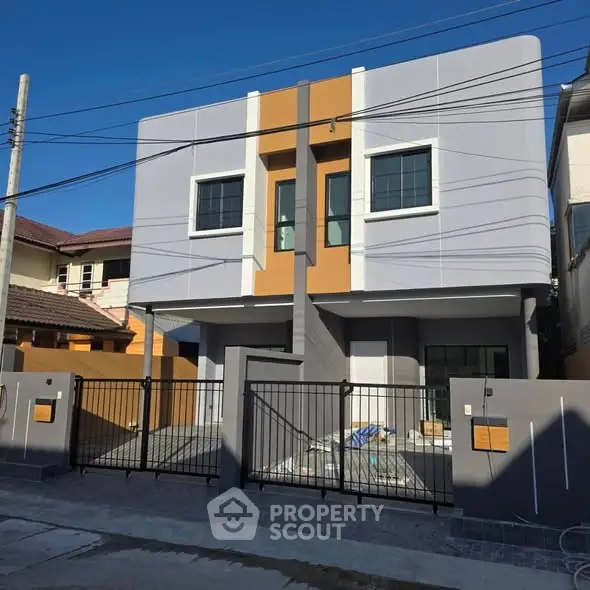 Modern two-story house with sleek design and gated entrance in a suburban neighborhood.