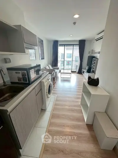 Modern open-plan living room with kitchen and balcony view, featuring sleek appliances and stylish decor.