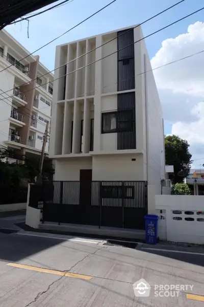 Modern minimalist three-story building with sleek facade and gated entrance in urban setting.