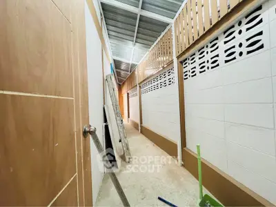 Narrow corridor with ladder and broom, showcasing simple construction details.