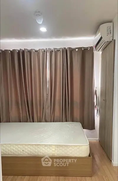 Cozy bedroom with wooden flooring and air conditioning, featuring a large window with curtains.