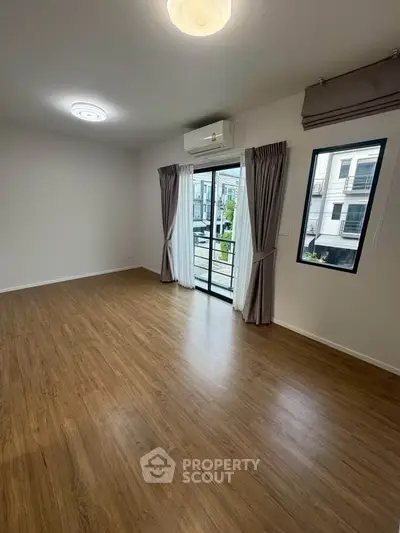Spacious empty room with wooden flooring and large window, perfect for customization.