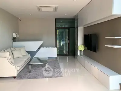 Modern living room with sleek furniture and large TV, featuring minimalist design and natural light.