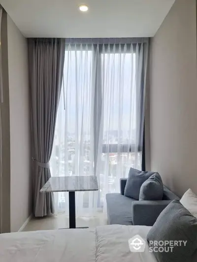 Cozy bedroom with city view, featuring a small sofa and elegant curtains.