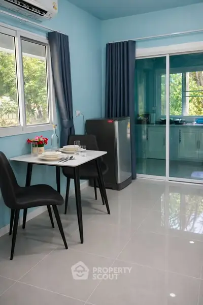 Modern dining area with sleek table and chairs, adjacent to a bright kitchen with large windows.
