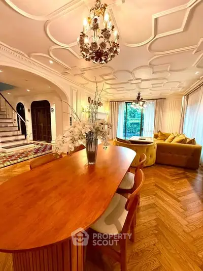 Luxurious living room with elegant chandelier and stylish wooden dining table, featuring a cozy seating area and large windows.