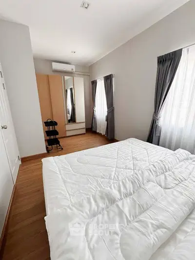 Spacious bedroom with wooden flooring, large windows, and modern furnishings for a cozy living experience.