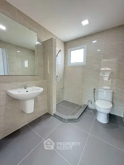 Modern bathroom with sleek fixtures and neutral tiles, featuring a shower and large mirror.