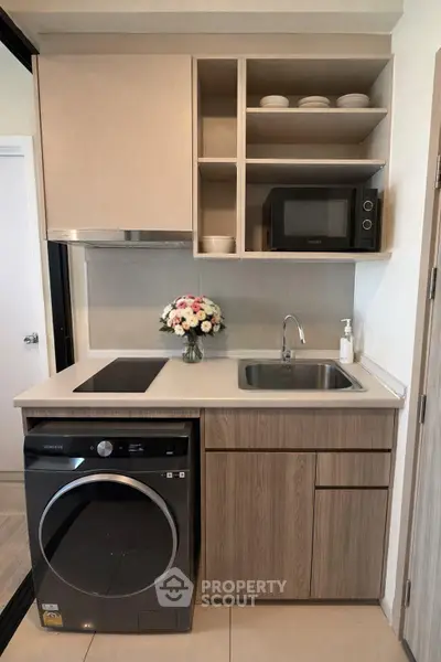 Modern compact kitchen with washing machine and microwave, featuring sleek cabinetry and stylish decor.