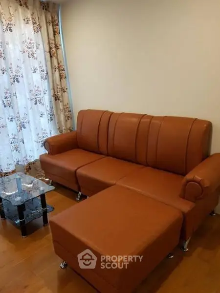 Cozy living room with stylish brown leather sofa and floral curtains, perfect for relaxation.