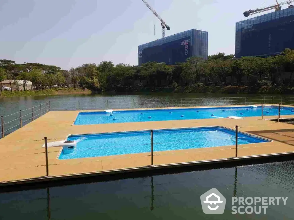 Luxurious outdoor swimming pool with crystal clear water, surrounded by a serene lake and modern high-rise buildings, offering an oasis of relaxation in a bustling cityscape.