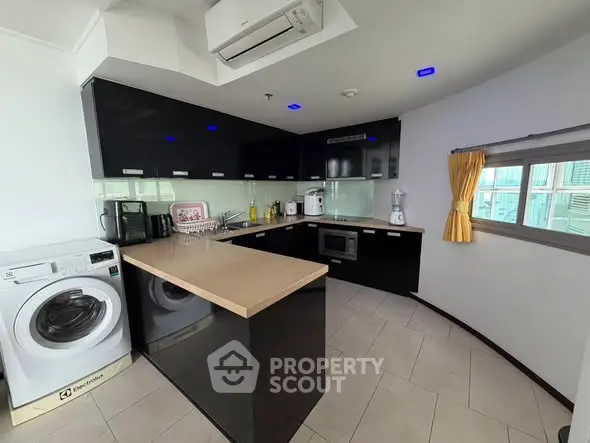 Modern kitchen with sleek black cabinets, integrated appliances, and a washing machine, offering a stylish cooking space.