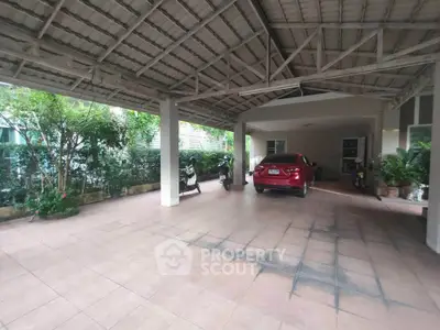 Spacious covered parking area with car and motorbikes, surrounded by greenery.